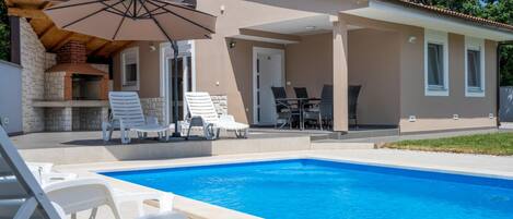 A poolside area with a barbecue, lounge chairs, and a covered patio.