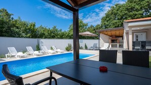 A covered outdoor area with a pool, lounge chairs, and a table with chairs.