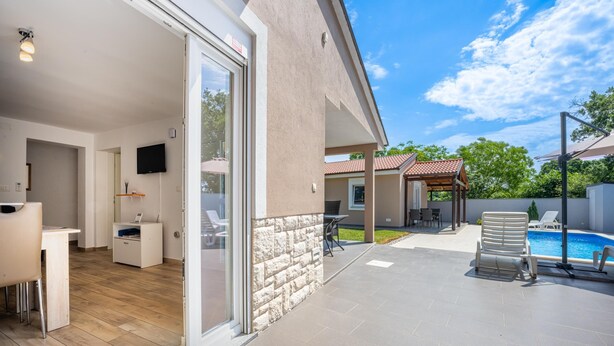 A modern house with a patio, a swimming pool, and a TV in the living area.