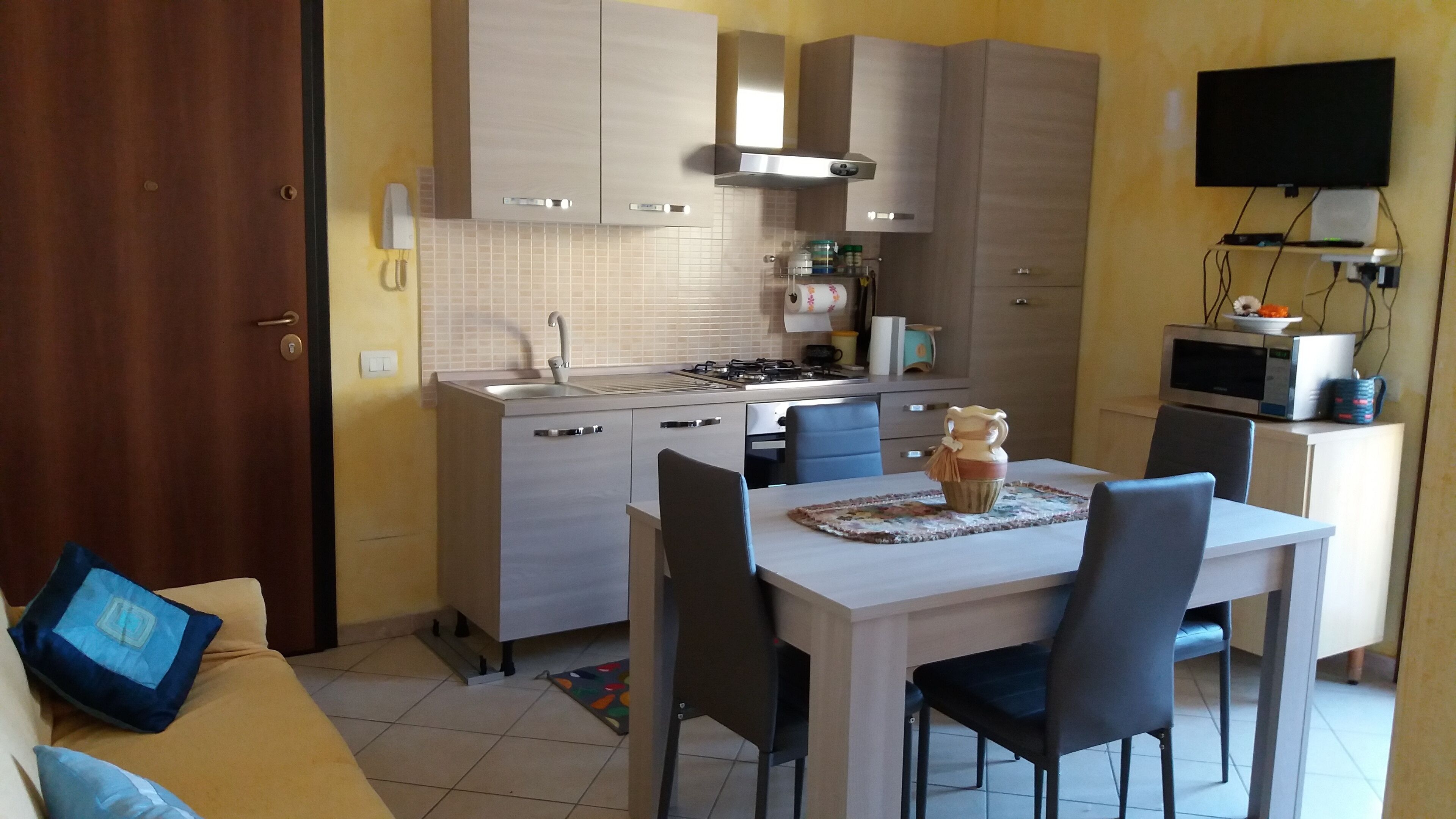 A compact kitchen with a dining area, a TV mounted on the wall, and a microwave on a cabinet.