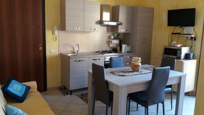 A compact kitchen with a dining area, a TV mounted on the wall, and a microwave on a cabinet. - Sole&Cuore is an elegant apartment accessorized and close to the beautiful CHIA   (Domus De Maria)
