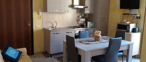 A compact kitchen with a dining area, a TV mounted on the wall, and a microwave on a cabinet.