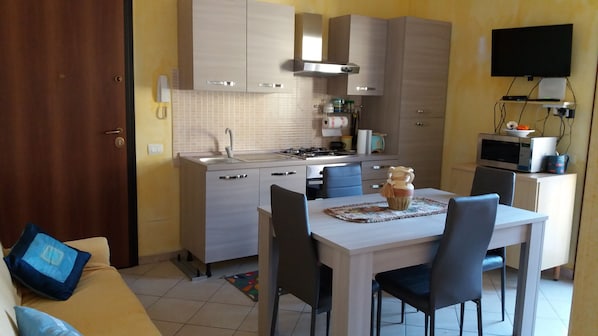 A compact kitchen with a dining area, a TV mounted on the wall, and a microwave on a cabinet.