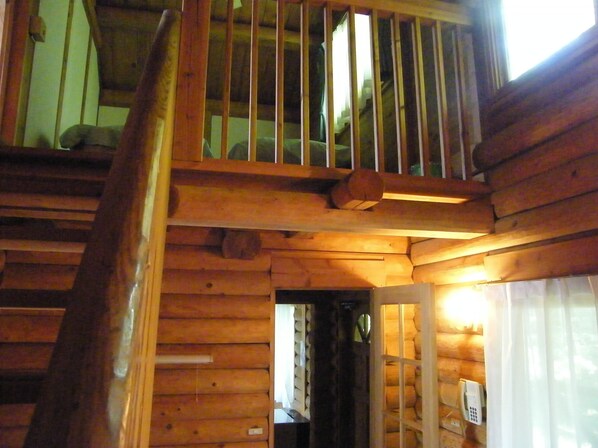Una escalera de madera conduce a un dormitorio superior con ventana y teléfono.