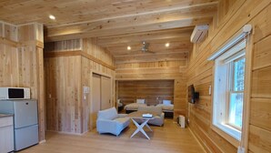 Ein Holzhütten-Innenraum mit einer Küchenzeile, einem Sofa, einem Tisch und einem an der Wand montierten Fernseher.