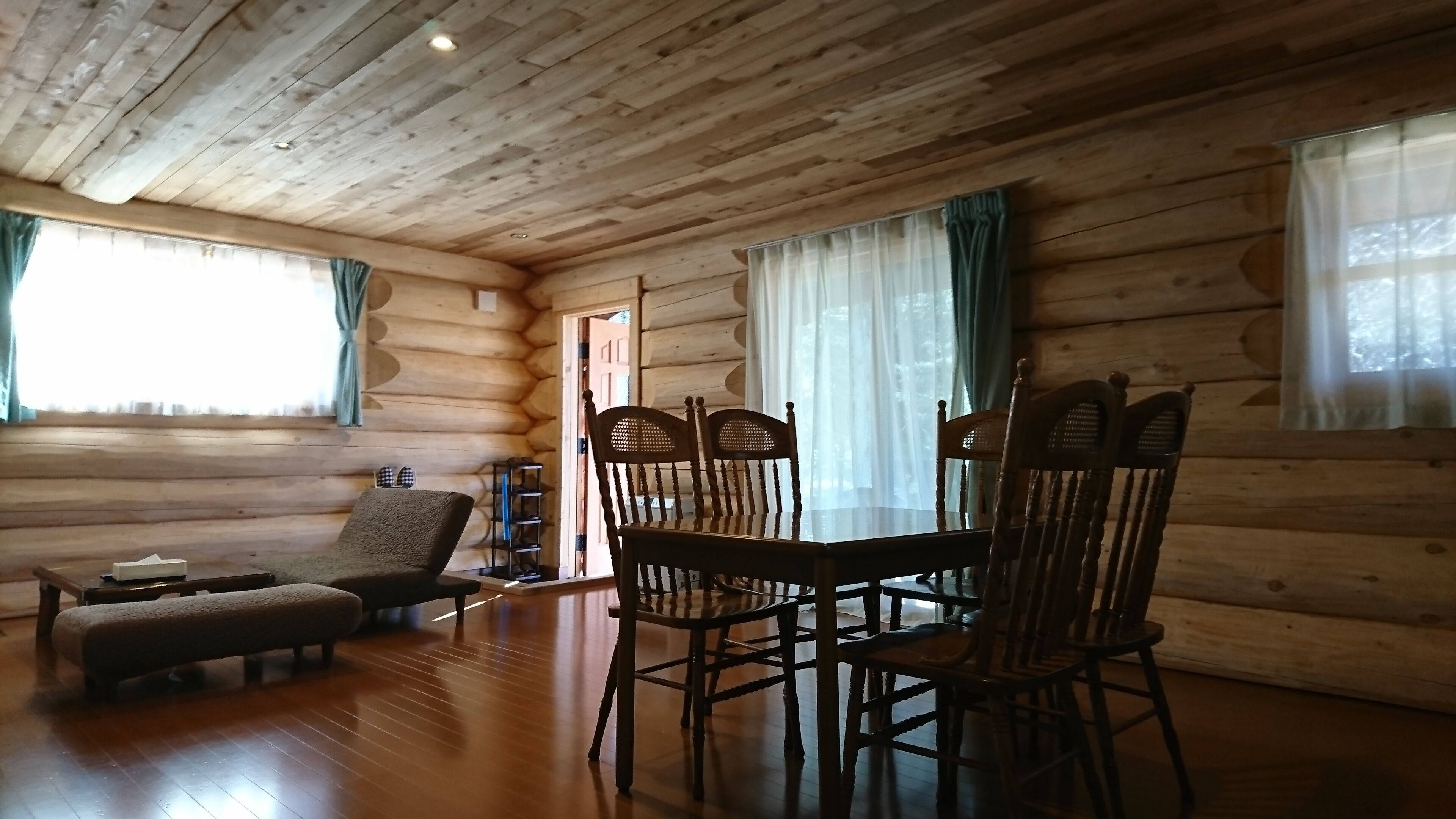 A log cabin interior with a wooden dining table, four chairs, a sofa, and a bench.