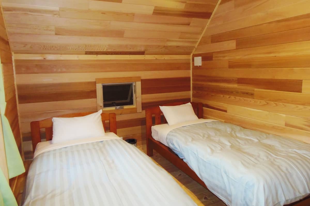 Eine Hütte mit zwei Einzelbetten, Holzwänden, einem kleinen Fenster und einem an der Wand befestigten Fernseher.