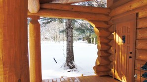 Der Eingang einer Holzhütte mit einem mit Schnee bedeckten Deck und einer Tür, die auf eine verschneite Landschaft führt.