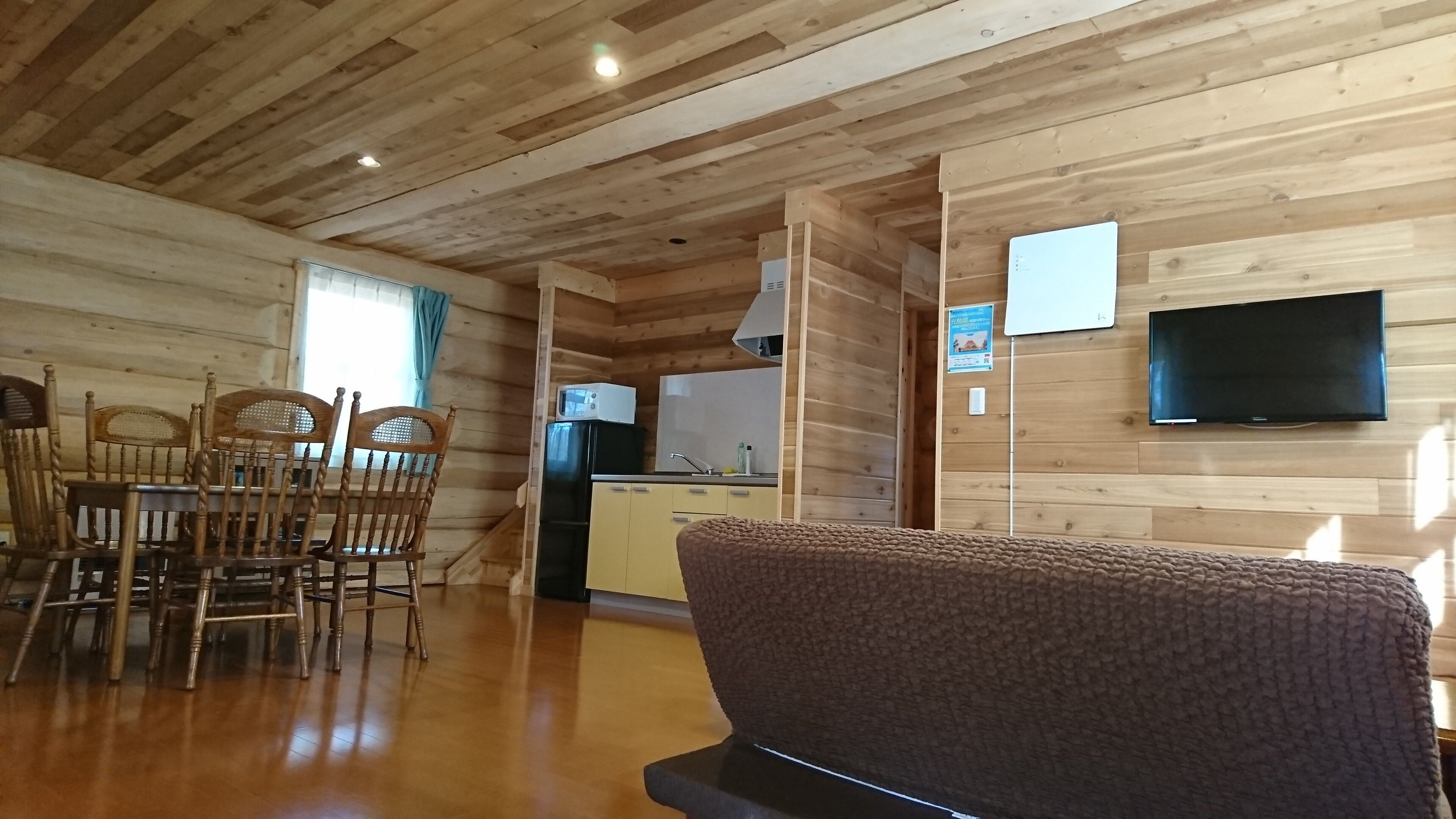 Ein Holzinnenraum mit Essbereich, Küche und einem an der Wand montierten Fernseher.