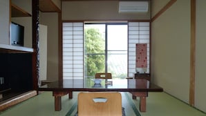 A traditional Japanese room with tatami flooring, a low table, a wooden chair, and sliding shoji doors. - Hotel Yoshino (Ito)