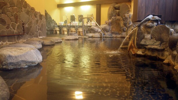 A stone bath area with a water feature, benches, and a stone wall. - Hotel Yoshino (Ito)
