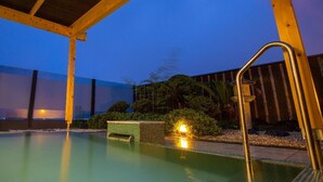 A swimming pool with a wooden deck and a covered area, surrounded by greenery and a building in the background. - Hotel Yoshino (Ito)