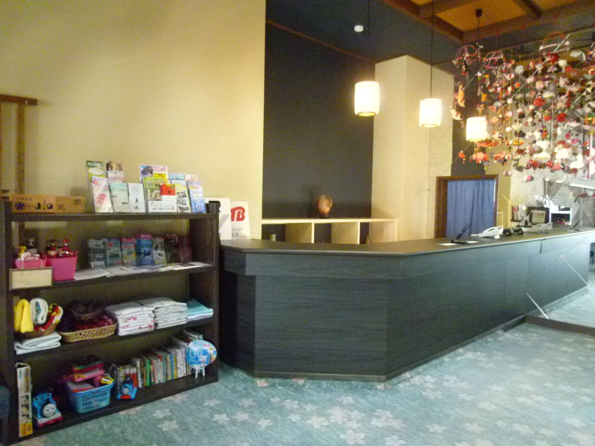 A reception desk with a dark counter, shelves with various items, and a wall decorated with hanging ornaments.