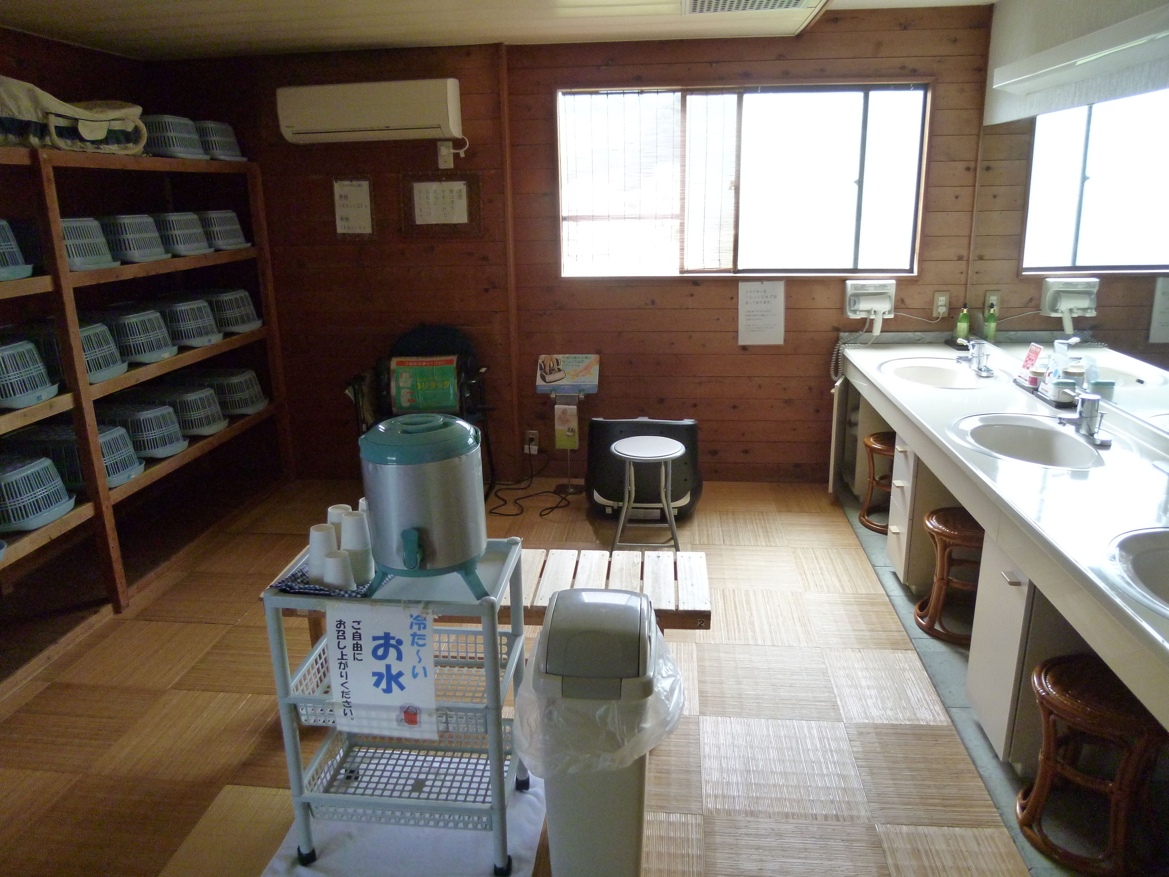 A kitchen with wooden walls, a sink, and a stove. There are shelves with baskets and a trash can.