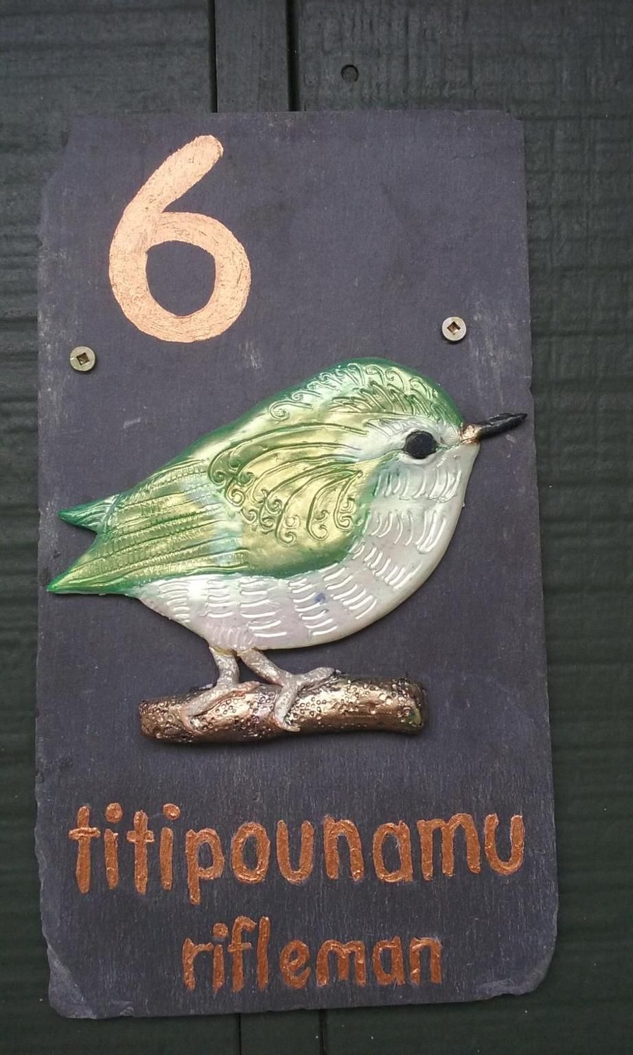 A house number sign with a bird illustration and the text 'titi pounamu rifleman'.