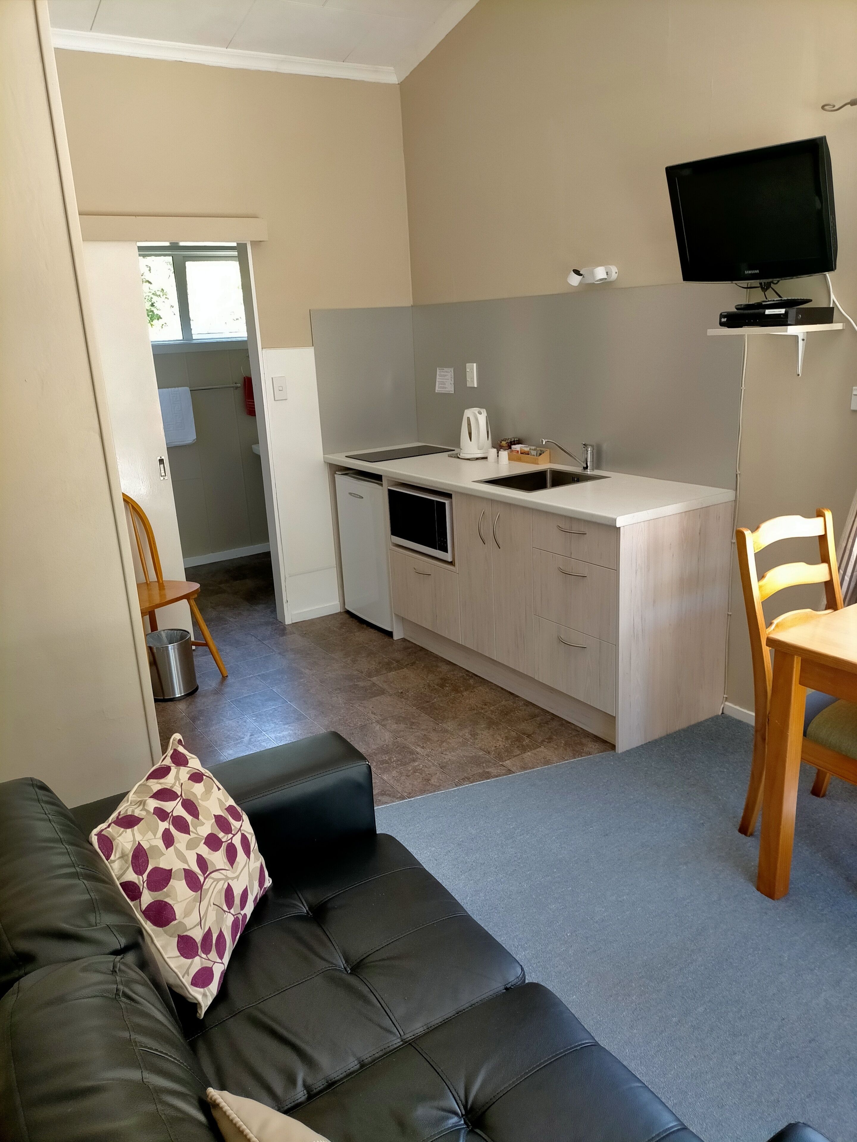 Un espacio habitable compacto con kitchenette, un sofá, zona de comedor y televisor.