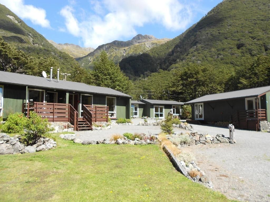 Una cabaña con un sendero de piedra que conduce a una terraza de madera, rodeada de exuberante vegetación y montañas.