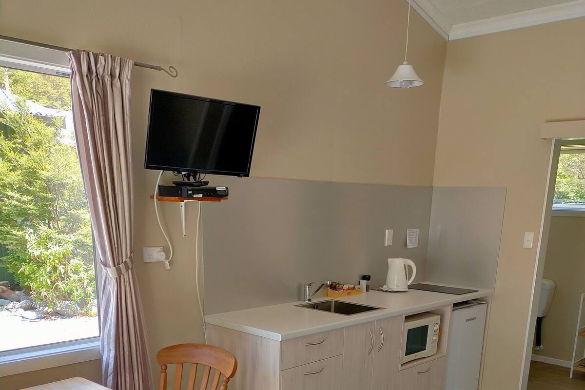 Een kleine keuken met een ingebouwde magnetron, een spoelbak en een televisie erboven.