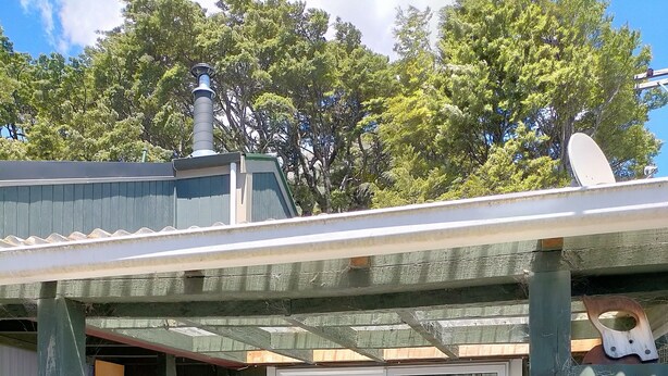 Un bâtiment à l’extérieur verdoyant, doté d’une cheminée et d’une antenne parabolique.