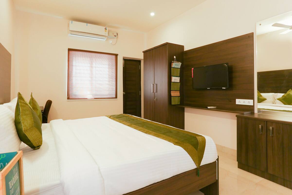 A hotel room with a bed, a TV, a wardrobe, and a window with blinds.