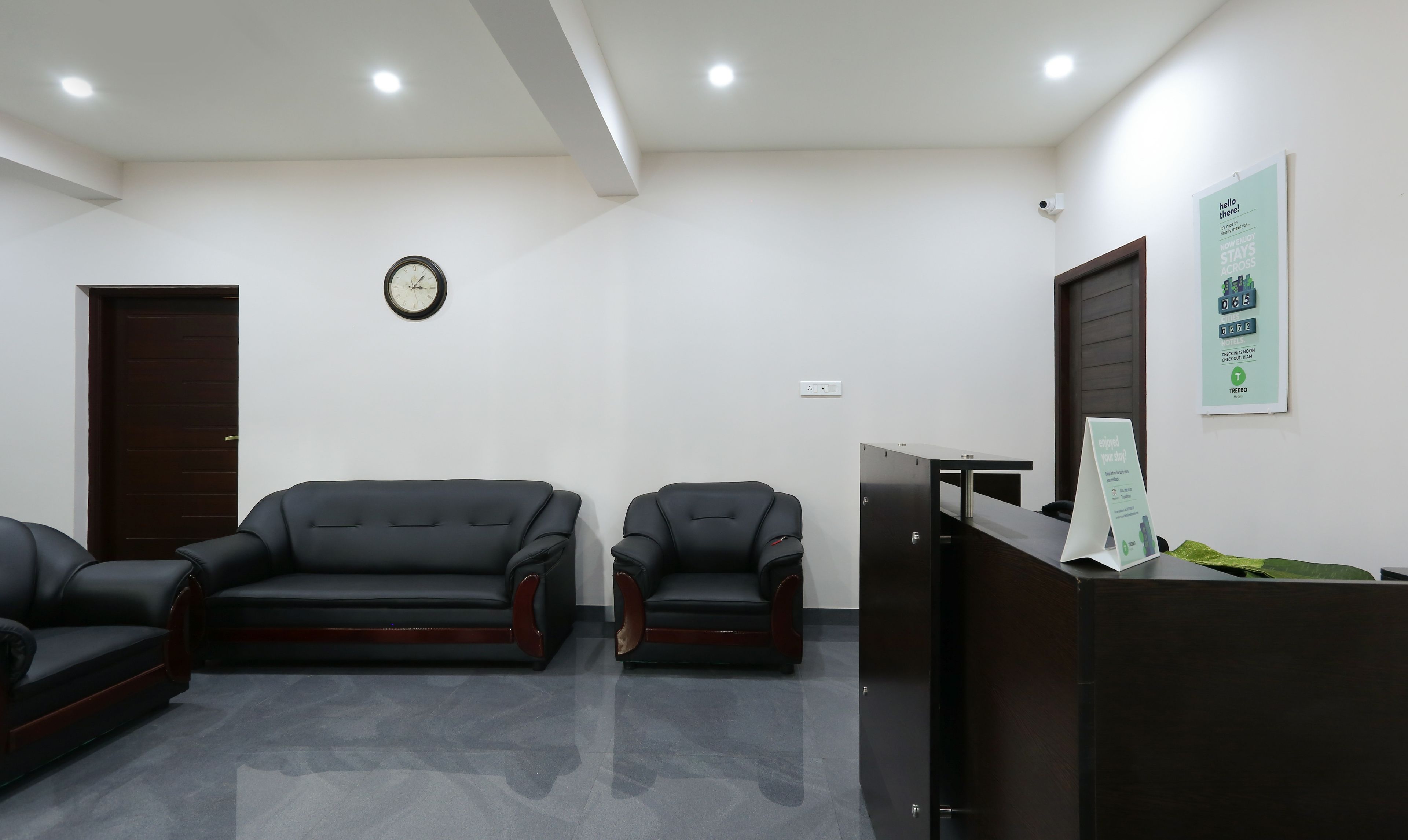 A reception area with a dark wooden desk, two black leather sofas, a wall clock, and a sign with a message.