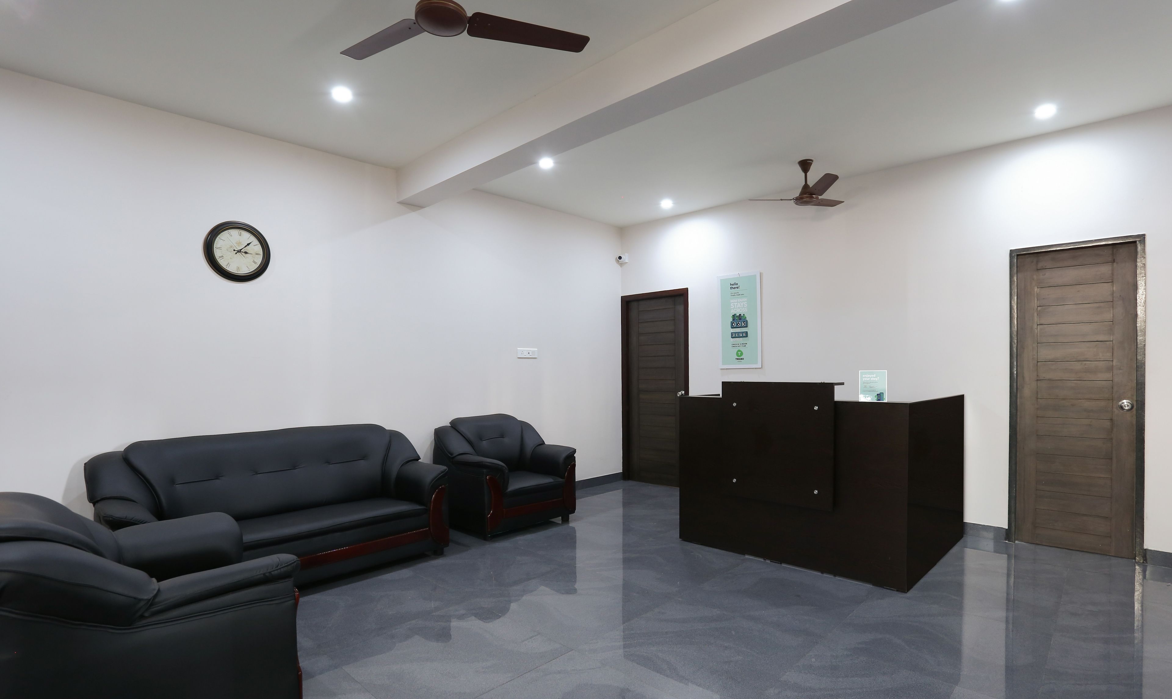 A reception area with a reception desk, two black sofas, a clock, and two ceiling fans.