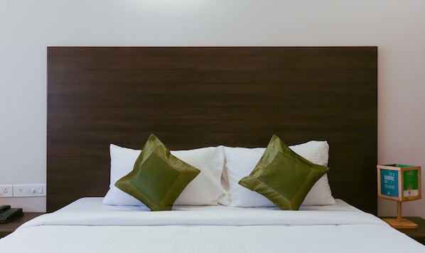 A hotel room with a large wooden headboard, white bedding, and two green pillows.