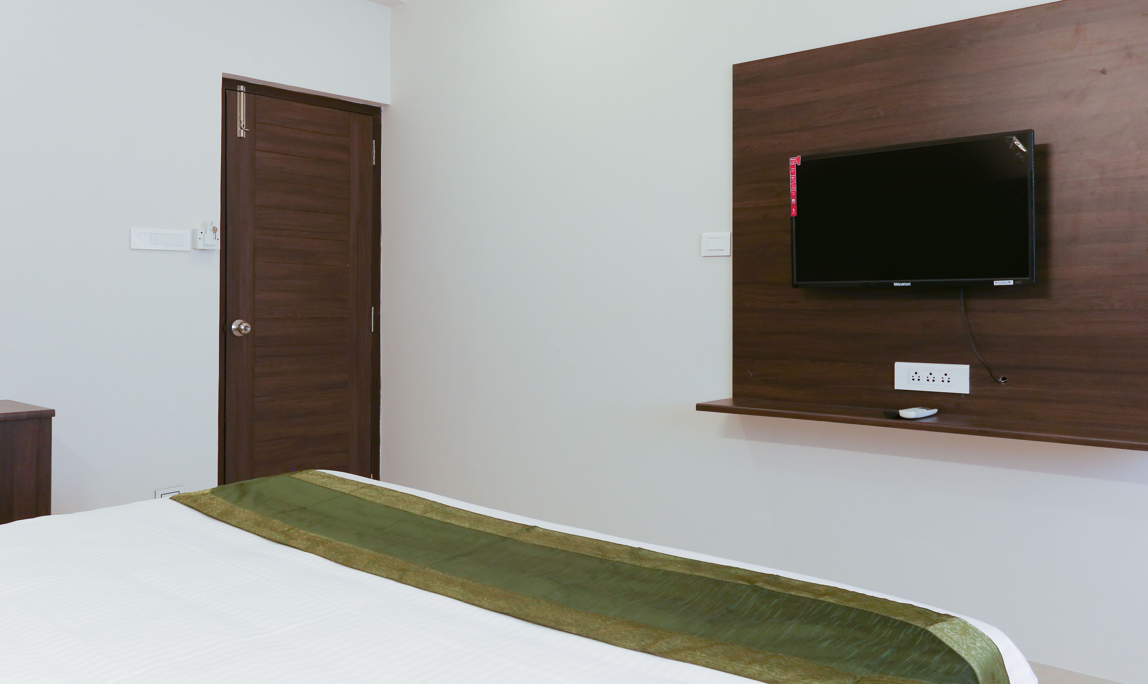 Ein Schlafzimmer mit einem Bett, einem Holzschrank, einem wandmontierten Fernseher und einer Steckdose.