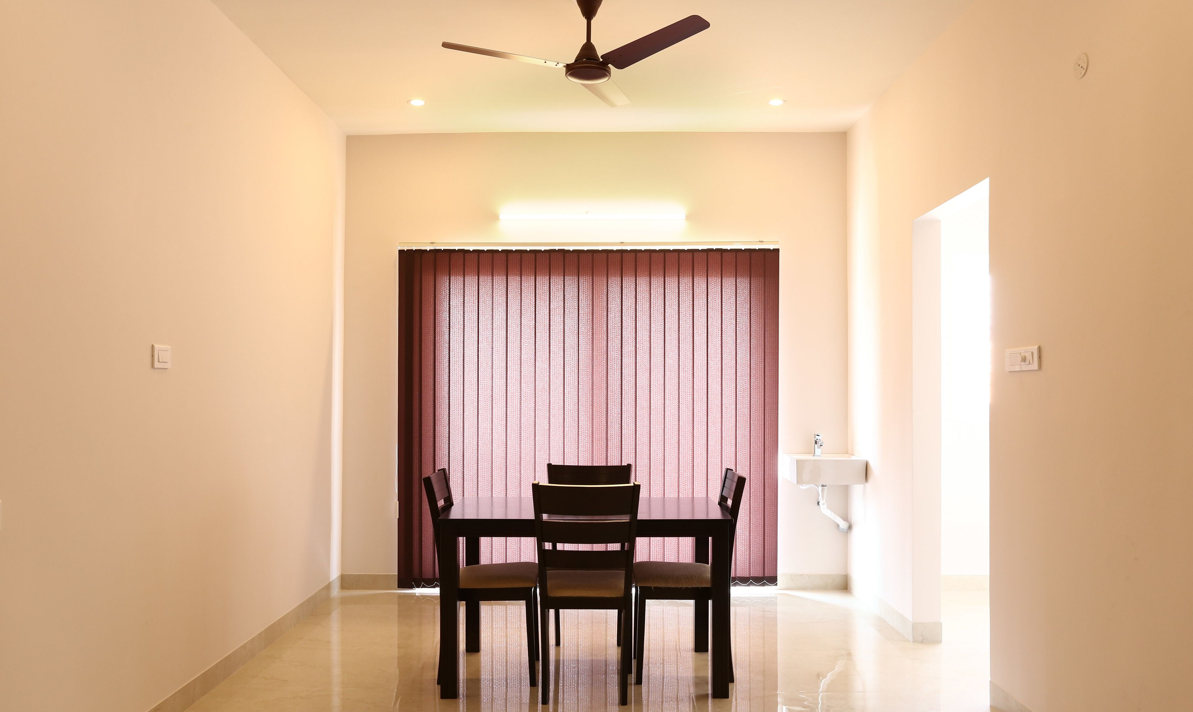 A dining area with a ceiling fan, a table with chairs, a window with curtains, and a wall-mounted light fixture.