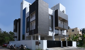 A modern multi-story residential building with balconies, a gated entrance, and parked motorcycles.