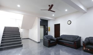A reception area with a staircase, a ceiling fan, a clock, and two leather sofas.