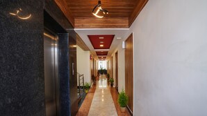 A hallway with a marble floor, wooden ceiling, and a modern light fixture. - Silicon Inn (Bengaluru)