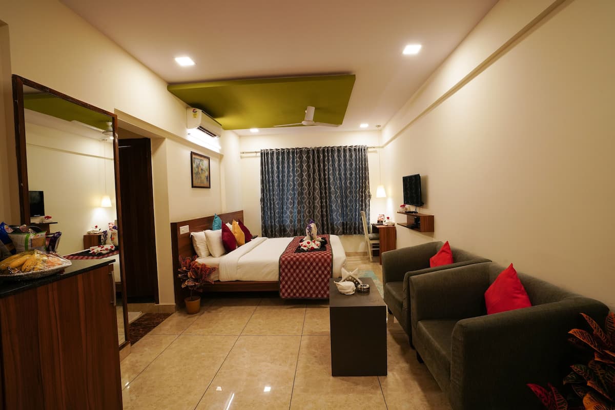 A hotel room with a bed, a sofa, a coffee table, a TV, and a dining area with a table and chairs.