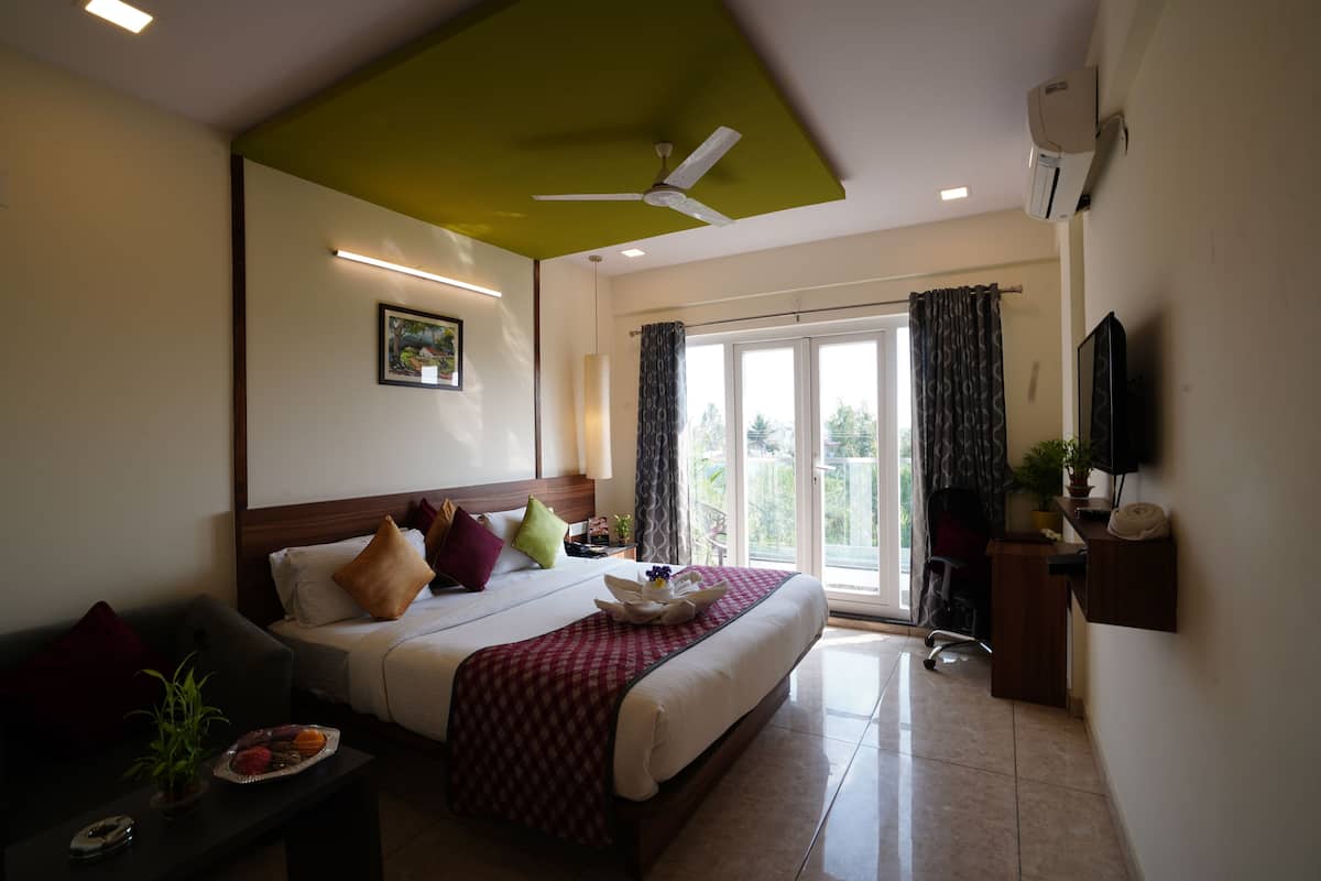 A hotel room with a large bed, a desk, a chair, a television, and a balcony with curtains.