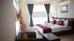A hotel room with a bed, a sofa, a small table, and a window with curtains. - Silicon Inn (Bengaluru)