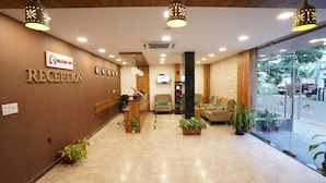 A reception area with a sign reading "RECEPTION," a reception desk, a television, and several potted plants. - Silicon Inn (Bengaluru)