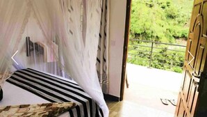 Un dormitorio con una cama, mosquitera y vistas a un balcón con vegetación.