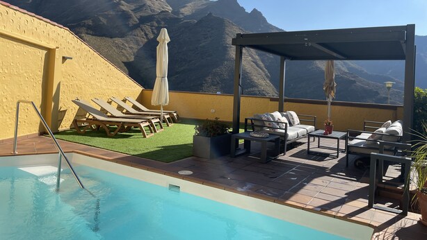 Un espace piscine aménagé sur le toit, avec des chaises longues et une pergola, offrant une vue sur un paysage montagneux.