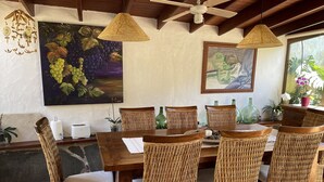 Un coin repas avec une table en bois et des chaises en osier, un ventilateur de plafond et des œuvres d’art accrochées aux murs.