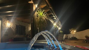 Une piscine dotée de plusieurs jets d’eau, entourée d’une terrasse en bois et de murs en pierre.