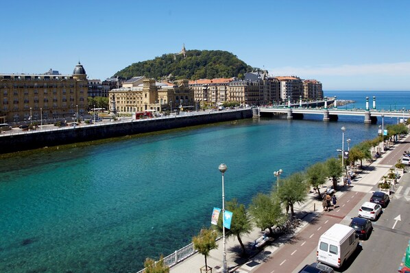 A coastal cityscape with a clear waterfront, a bridge, and buildings along the promenade.