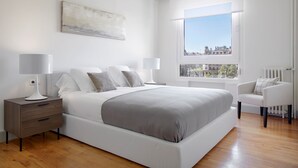 A modern bedroom with a large bed, bedside tables, a chair, and a window with a city view. - Okendo by FeelFree Rentals (San Sebastián)