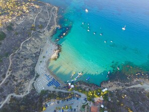 Vue aérienne d’une zone côtière avec une plage, des bateaux et un port de plaisance.