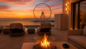 Terraza en la azotea con un brasero, asientos y vistas a una noria al atardecer.