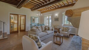 A spacious living room with a high ceiling, wooden beams, a sofa set, a coffee table, and a view of the kitchen through an open door. - Lovely villa with private pool, located in close distance to Cortona  (Ossaia)