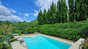 A rectangular swimming pool with clear blue water, surrounded by a stone deck and bordered by lush green hedges and tall trees. - Lovely villa with private pool, located in close distance to Cortona  (Ossaia)