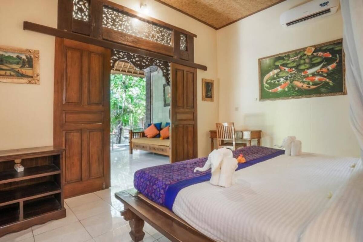 A hotel room with a bed, a wooden bench, a small table, and a chair.