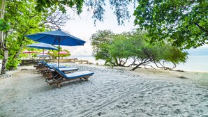 Ein Strand mit Liegestühlen und Sonnenschirmen, ein sandiger Uferstreifen und Bäume.