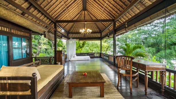 Eine großzügige Veranda mit einem Reetdach, Holzmöbeln und Blick auf üppiges Grün.