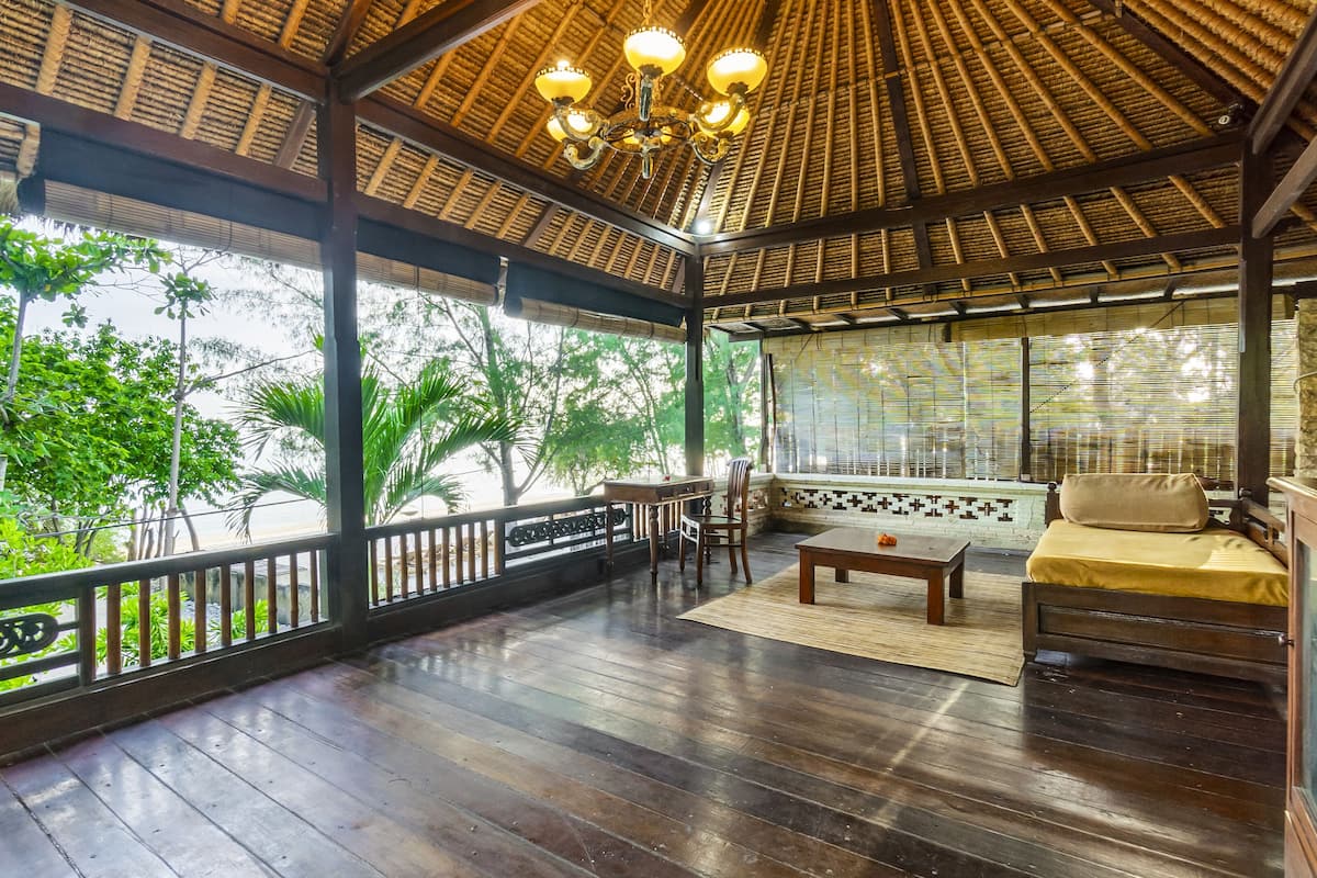 A covered outdoor seating area with wooden flooring, a table, chairs, and a sofa.